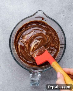 Thick chocolate mixture in a glass bowl being folded with a red spatula.