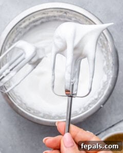 Electric mixer beaters holding glossy, stiff egg whites ready for folding.