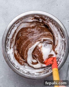 Mixing bowl with chocolate mixture being gently folded with a red spatula to combine egg whites and chocolate.