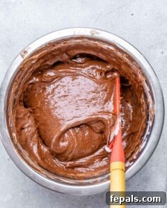 Mixing bowl filled with smooth chocolate soufflé batter being stirred with a red spatula.