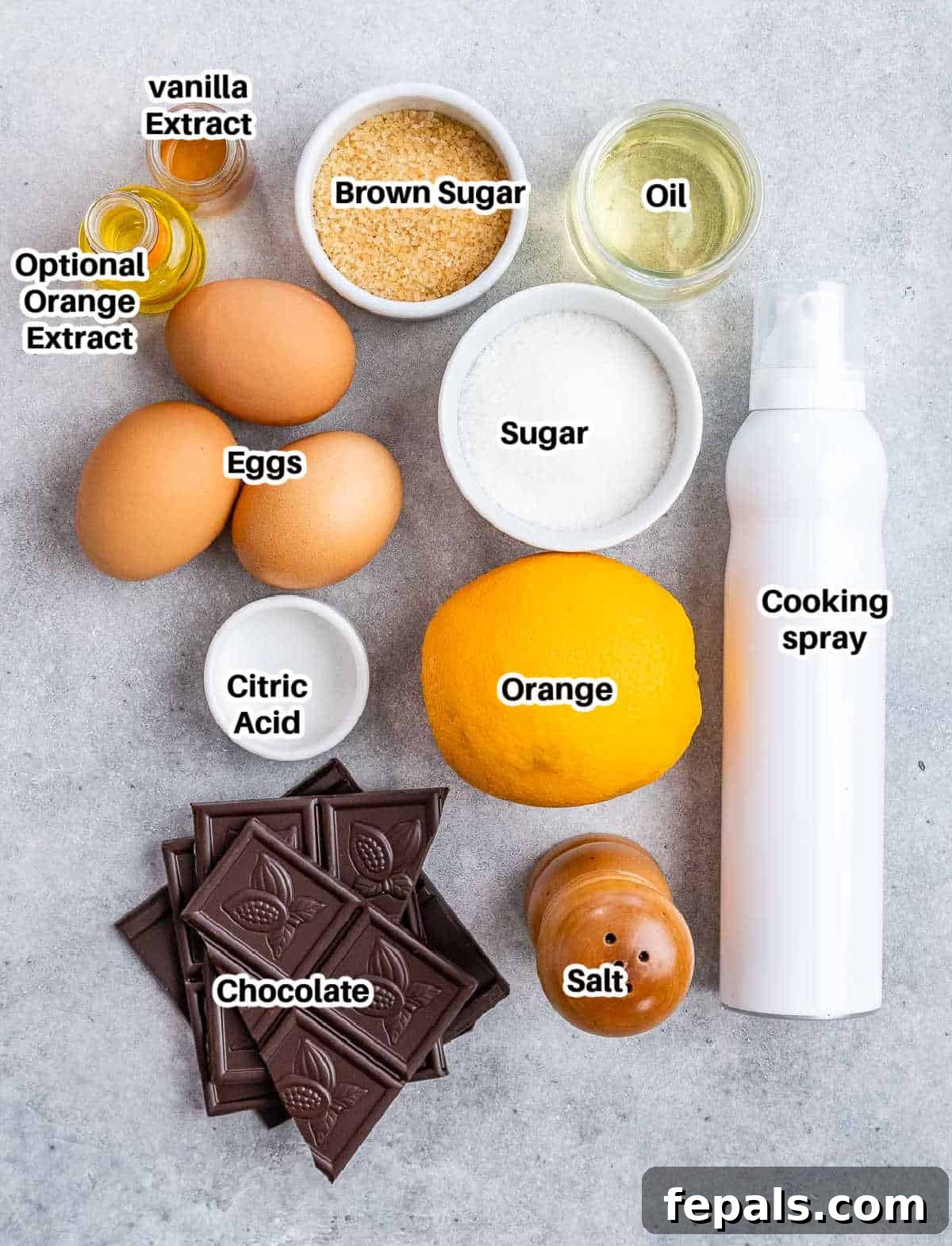 A selection of high-quality ingredients laid out on a clean surface, including chocolate bars, eggs, sugar, oil, vanilla extract, and an orange for zest, all ready for making chocolate soufflé.