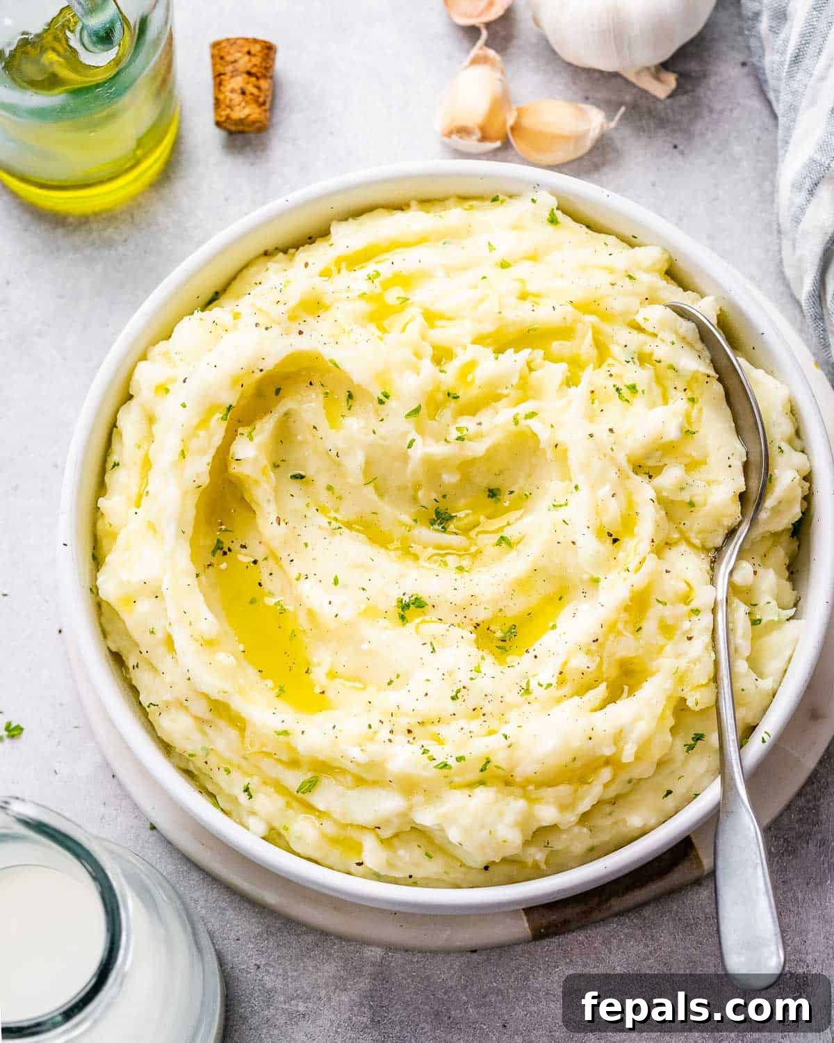 A small round bowl generously filled with perfectly creamy Boursin mashed potatoes, garnished with fresh green herbs.