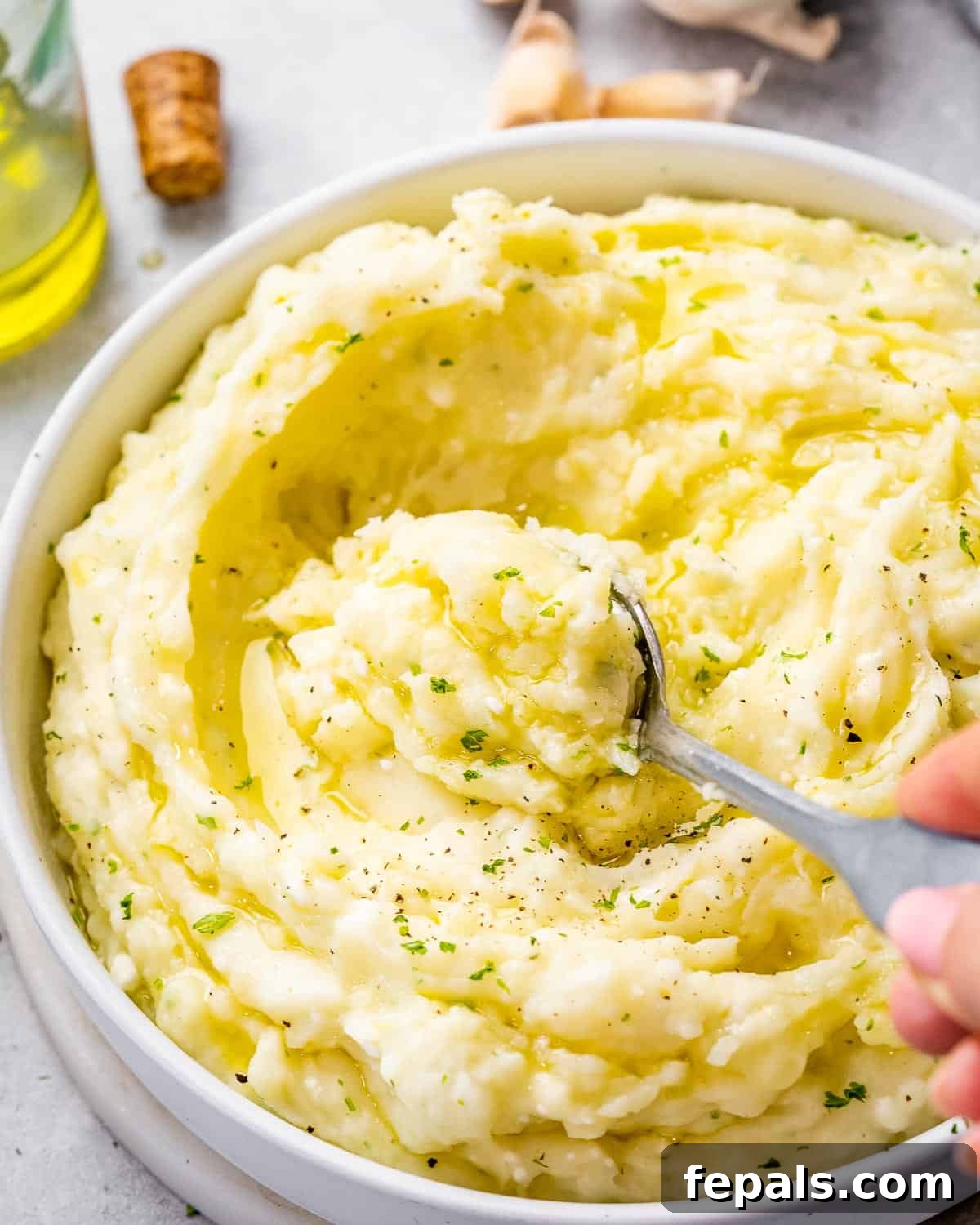 A large serving spoon stirring a bowl of creamy Boursin mashed potatoes, highlighting their smooth, rich texture and inviting warmth.