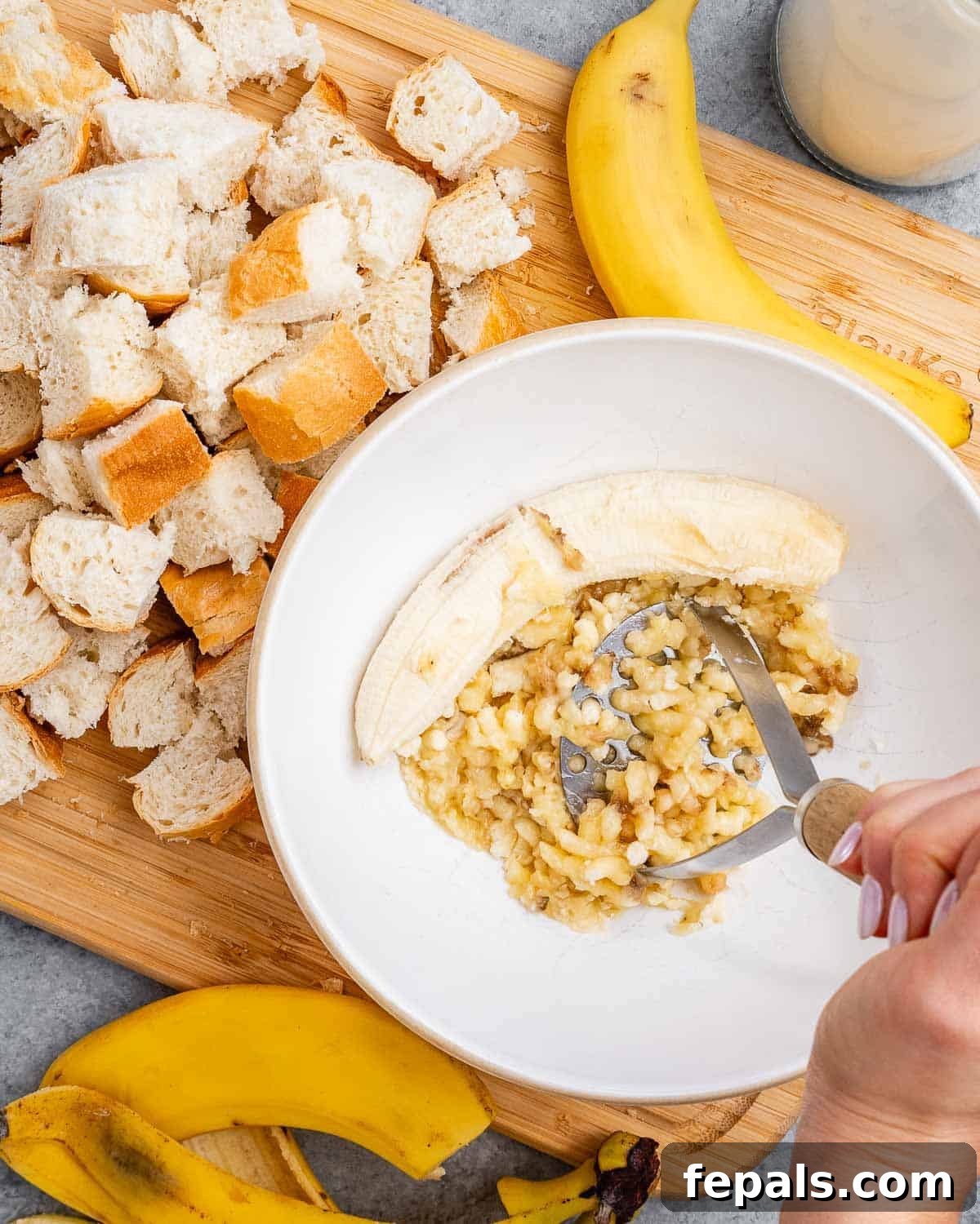 Hands mashing ripe bananas in a large bowl with a fork, preparing the base for homemade banana bread pudding.