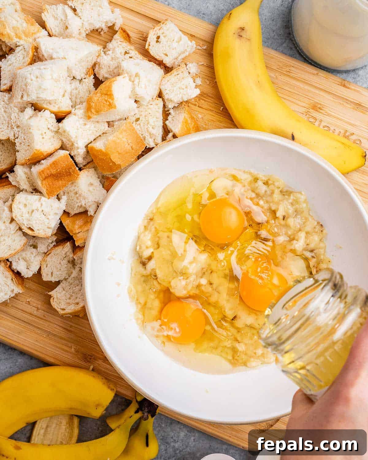 Eggs being carefully cracked and added into a bowl of mashed bananas, ready for whisking to create the custard mixture.