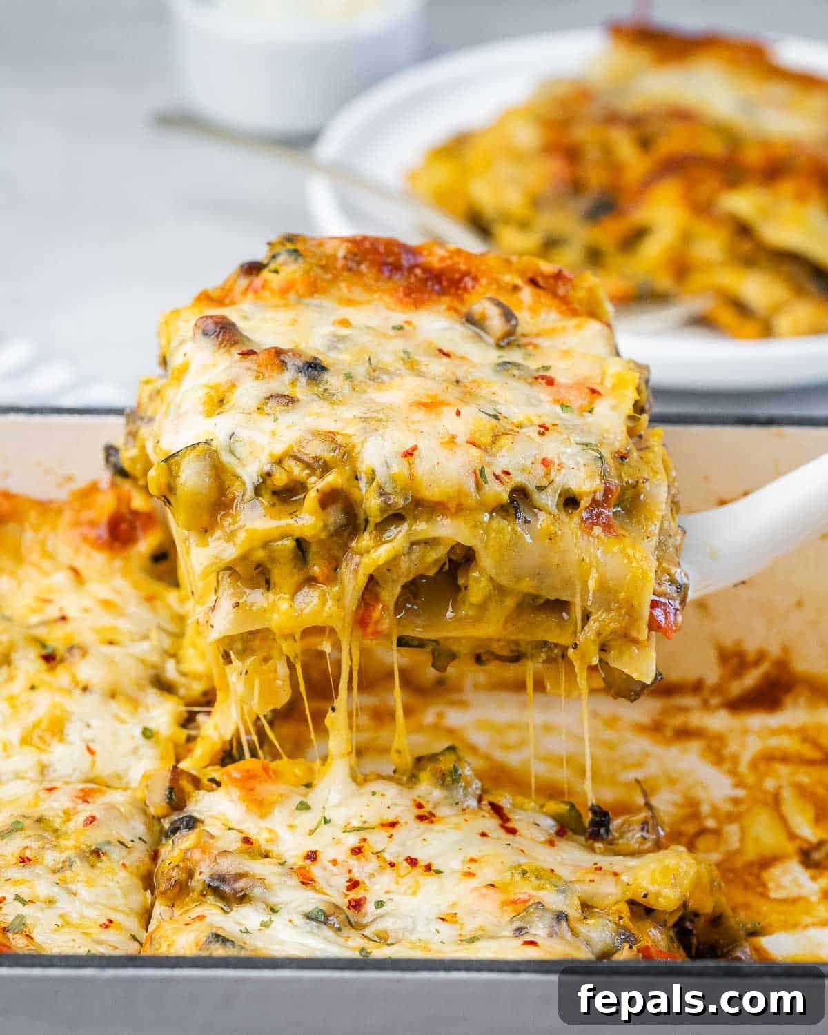 Velvety Butternut Squash Lasagna 2 A spatula lifting a gooey, cheesy piece of butternut squash lasagna from a baking dish with stretchy melted cheese pulling away, highlighting the rich layers.