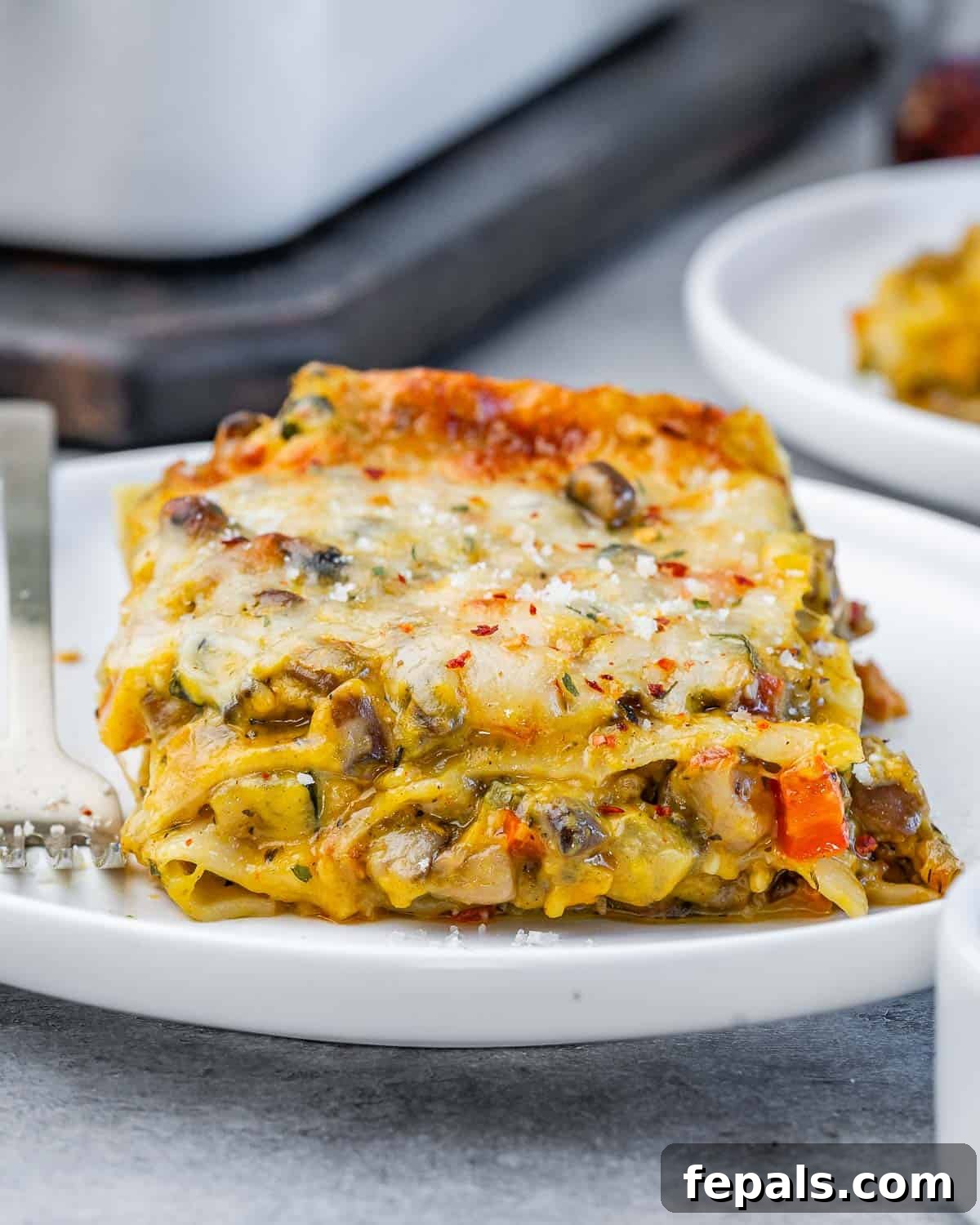 Velvety Butternut Squash Lasagna 6 Close-up of a perfectly baked slice of butternut squash lasagna showing creamy layers of noodles, sautéed vegetables, and melted golden cheese on a white plate, ready to be enjoyed.