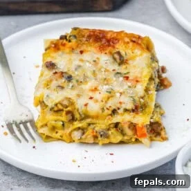 Velvety Butternut Squash Lasagna 8 A plated slice of butternut squash lasagna topped with melted mozzarella and fresh herbs, served alongside a fork on a clean white plate, ready to eat.