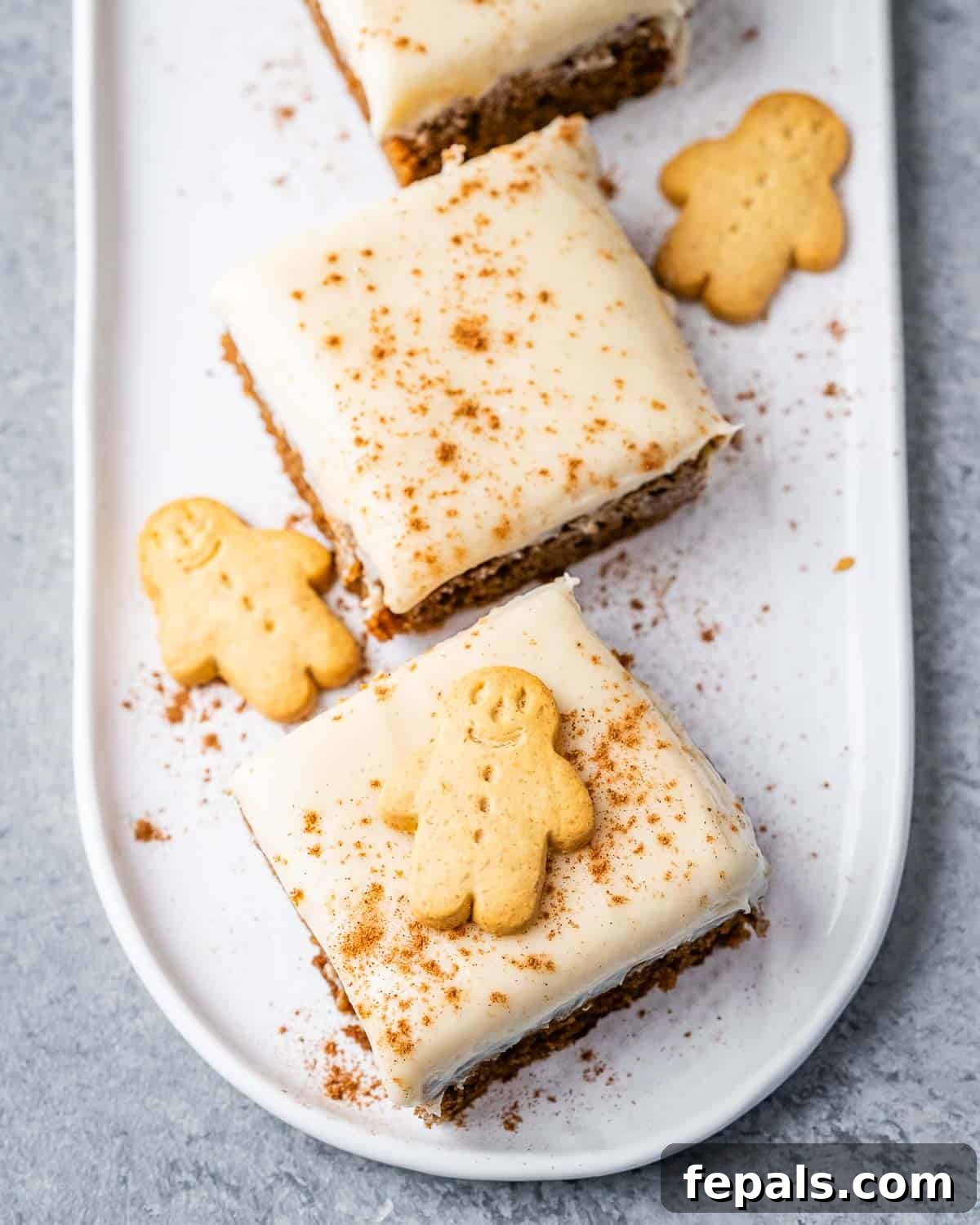Gingerbread cake squares on a plate with a gingerbread man on one of them is topped with a gingerbread man cookie.