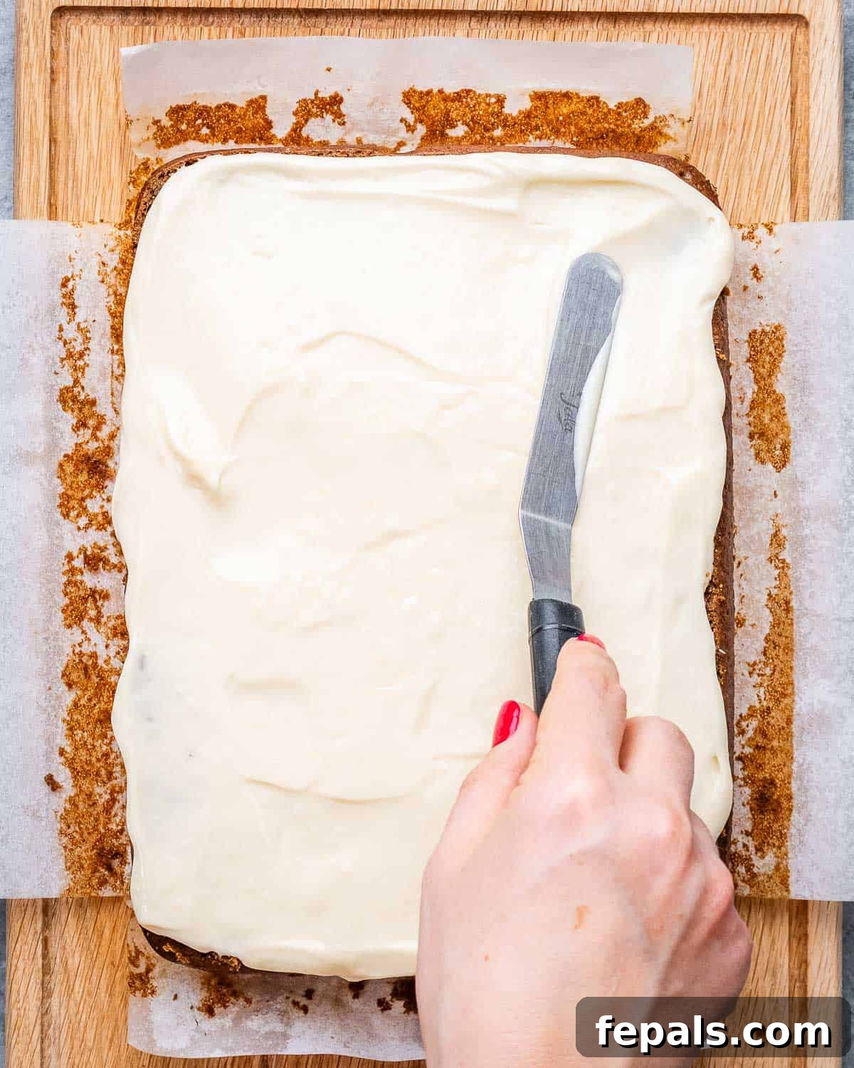 vanilla frosting being spread over gingerbread cake.