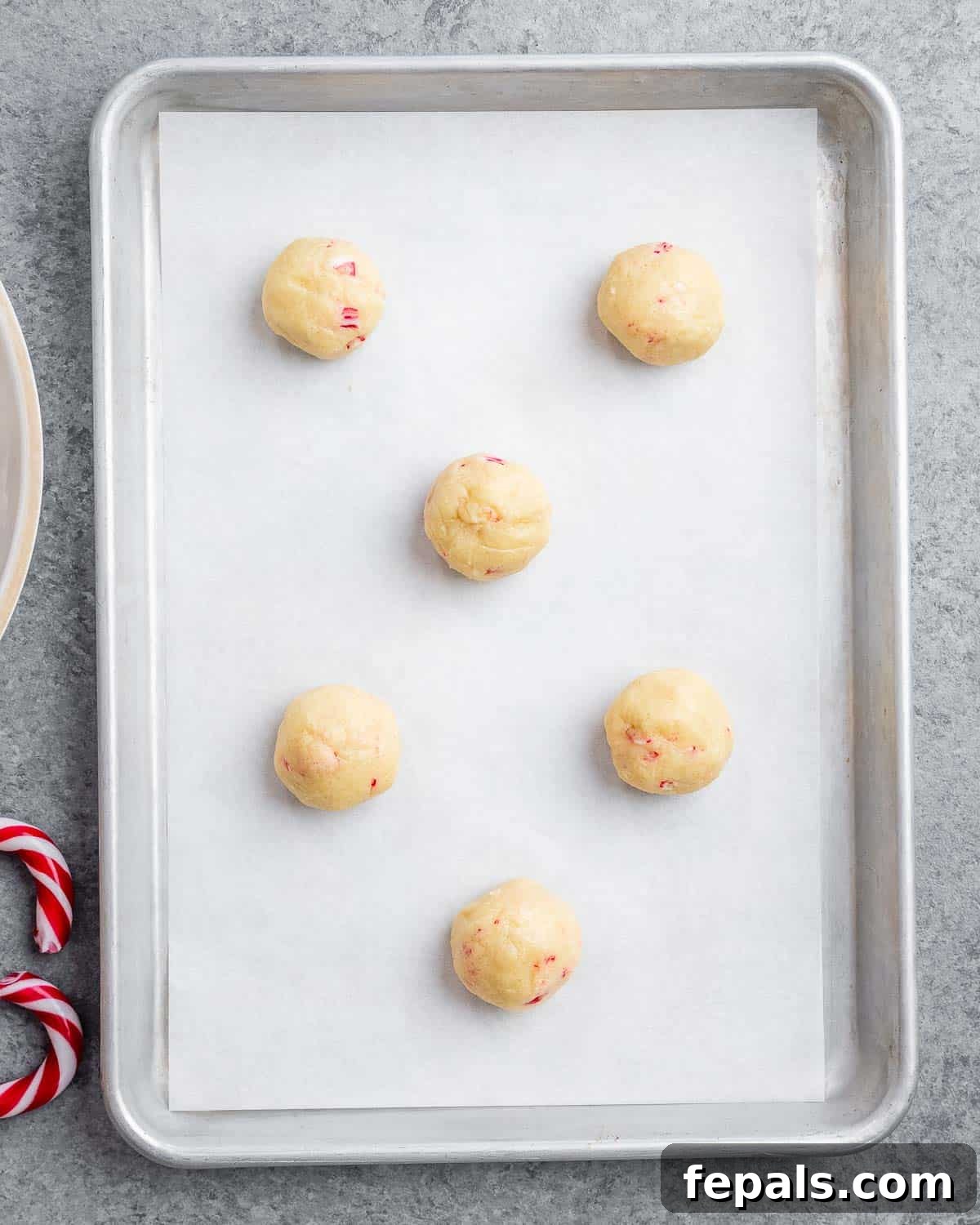 Uniform balls of peppermint cookie dough meticulously arranged on a parchment-lined baking sheet, awaiting their chilling period before baking.
