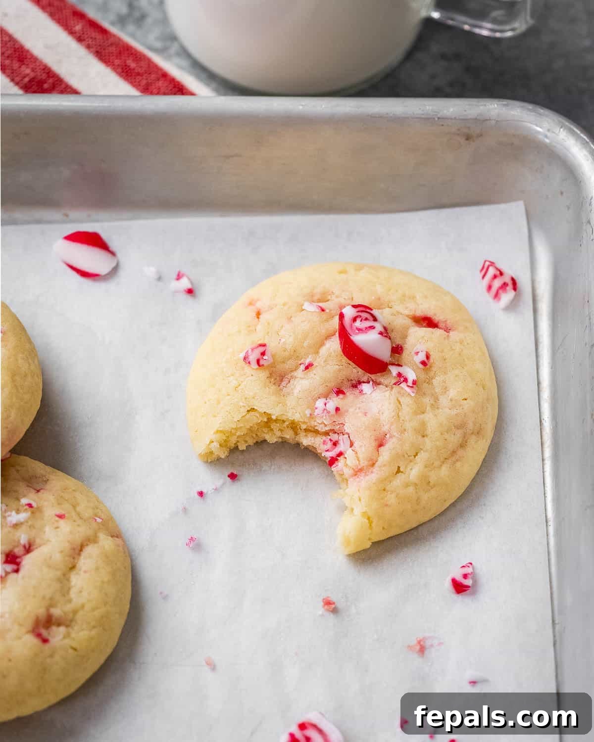 A freshly baked peppermint cookie with a small bite taken out, showcasing its soft interior and crunchy peppermint bits, resting on a baking sheet.