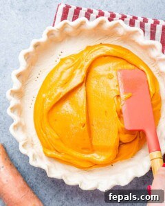 Unbaked pie being filled with orange sweet potato mixture using a red spatula.