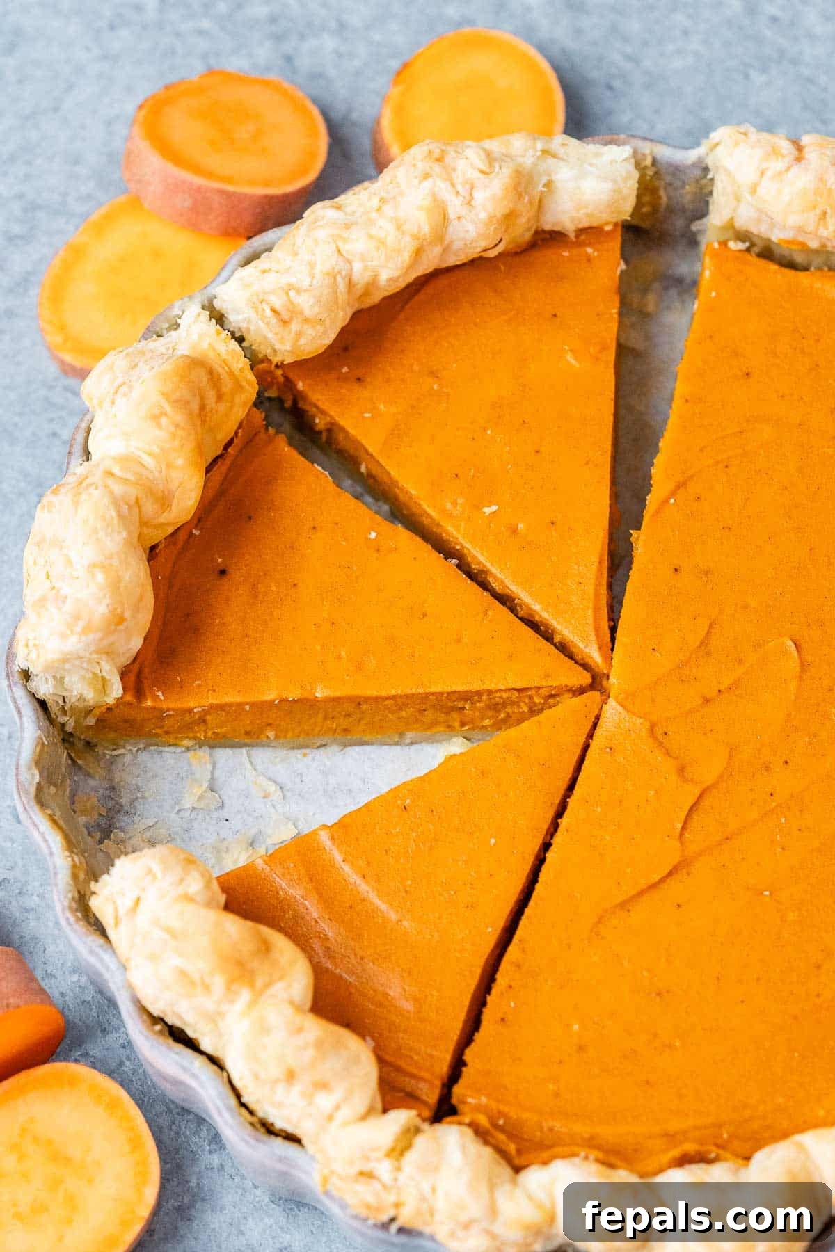 A whole sweet potato pie with several slices cut out, revealing the perfectly smooth orange filling and golden, flaky crust. It's ready for serving.