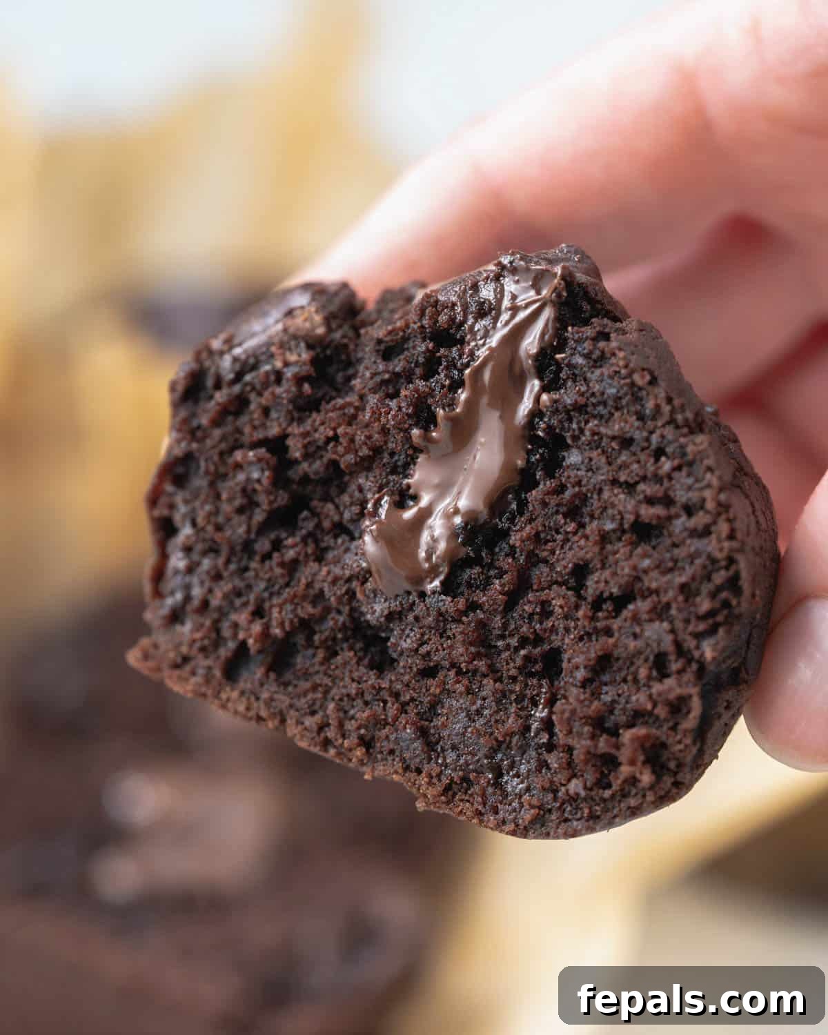 Olympian's Delight Chocolate Muffins 7 hand holding a chocolate muffin cut in half, revealing the luscious chocolate ganache filling in the middle.