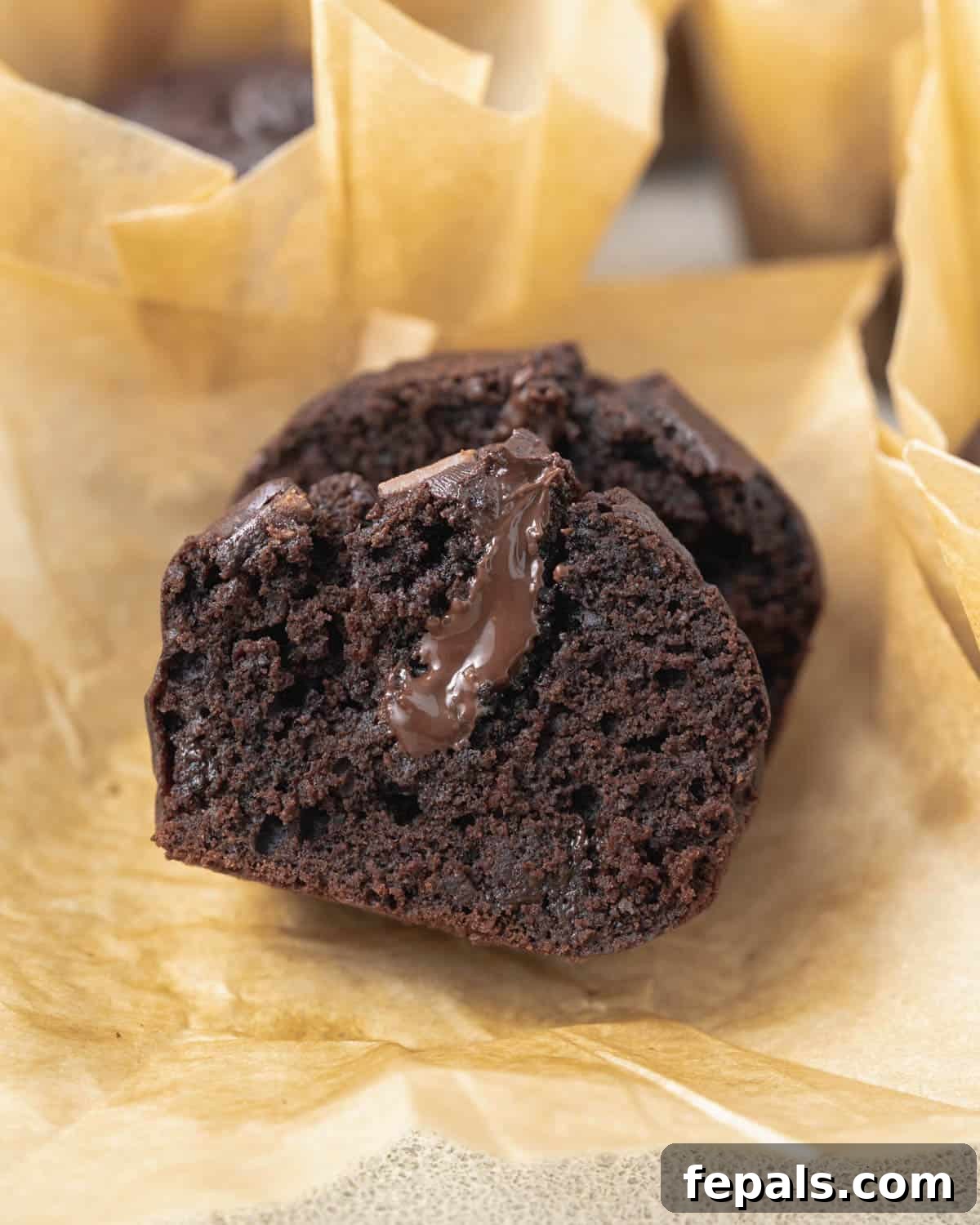 Olympian's Delight Chocolate Muffins 9 Chocolate muffins cut in half and placed on parchment paper, displaying the rich chocolate ganache center.