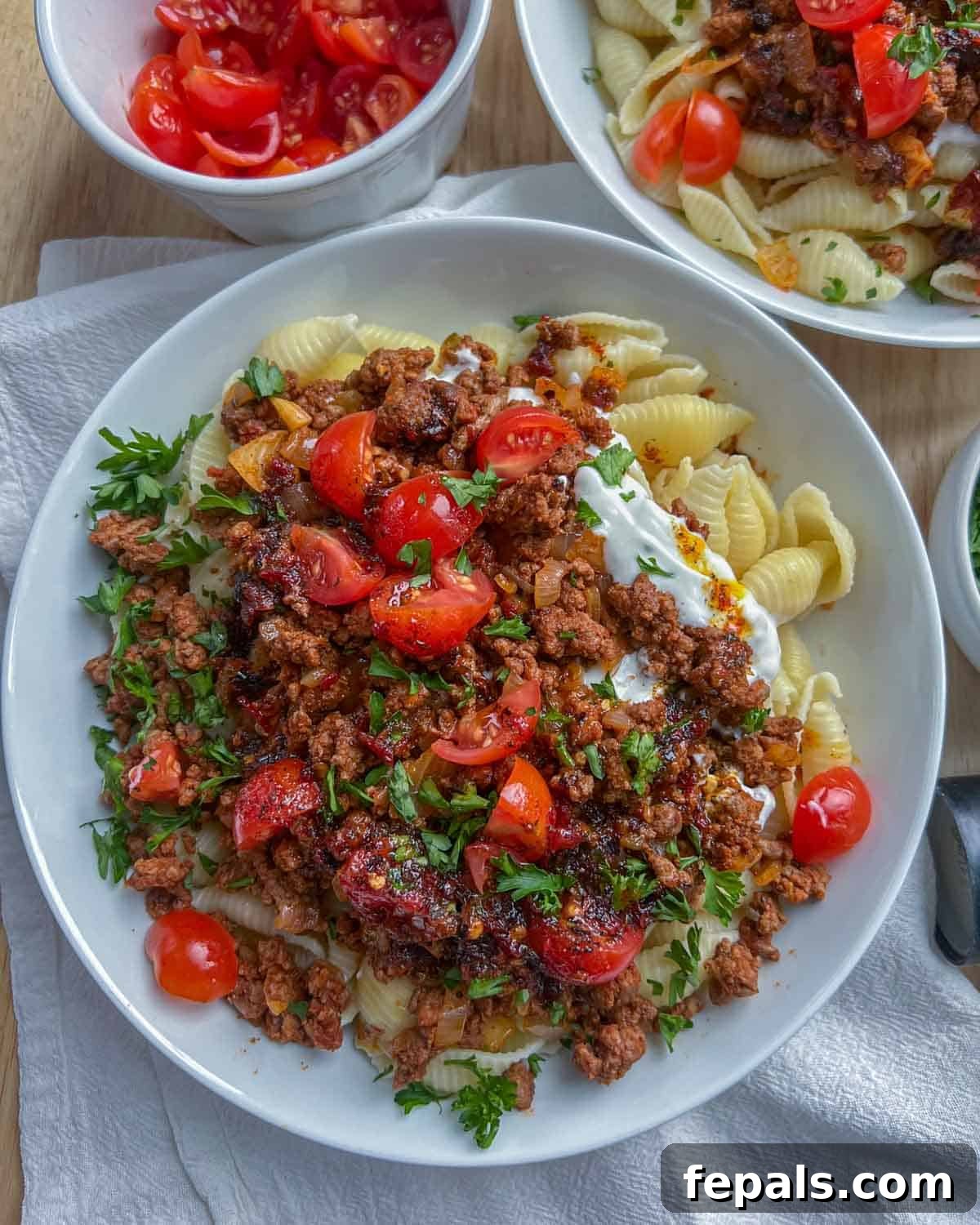 A beautiful white dish brimming with Turkish pasta, topped with perfectly seasoned ground beef, vibrant chopped tomatoes, and fresh parsley, ready to be enjoyed.