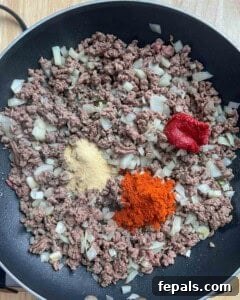 seasonings added over seared beef and onions in a pan.