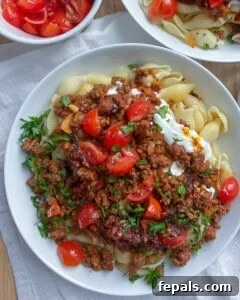 assembled Turkish pasta in a white dish topped with chopped tomatoes and parsley.