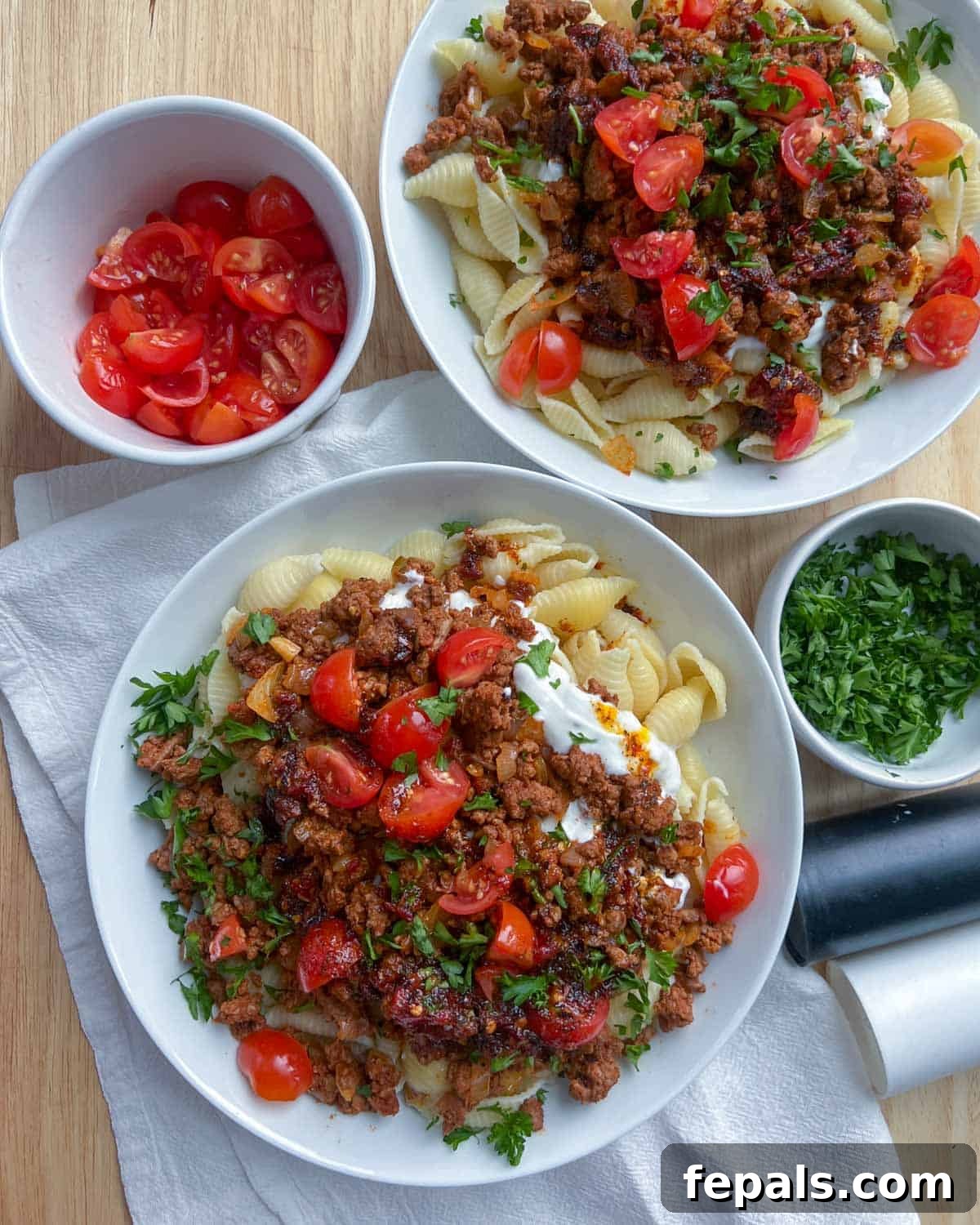 Two generous plates of Turkish pasta, beautifully arranged and ready to serve, with small bowls of fresh tomatoes and parsley for garnish.