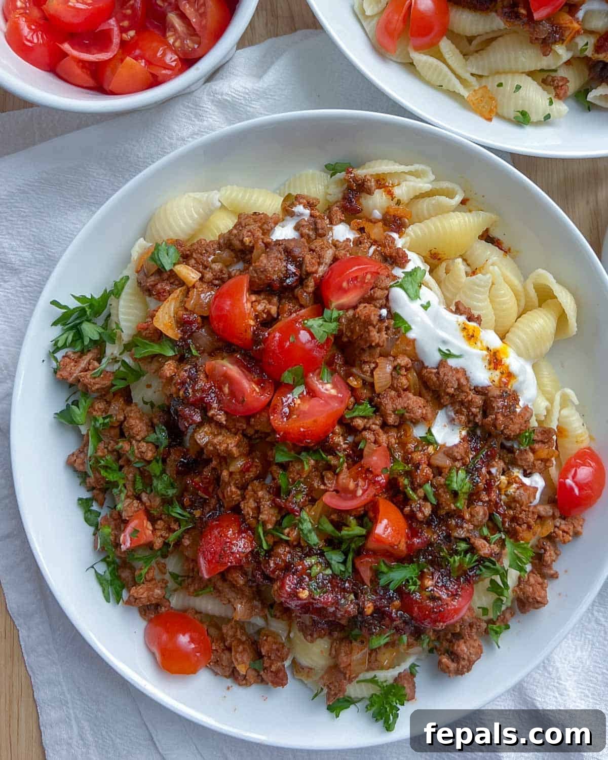 A perfectly plated dish of Turkish pasta, generously topped with seasoned ground beef, fresh chopped tomatoes, and aromatic parsley, ready for a satisfying meal.