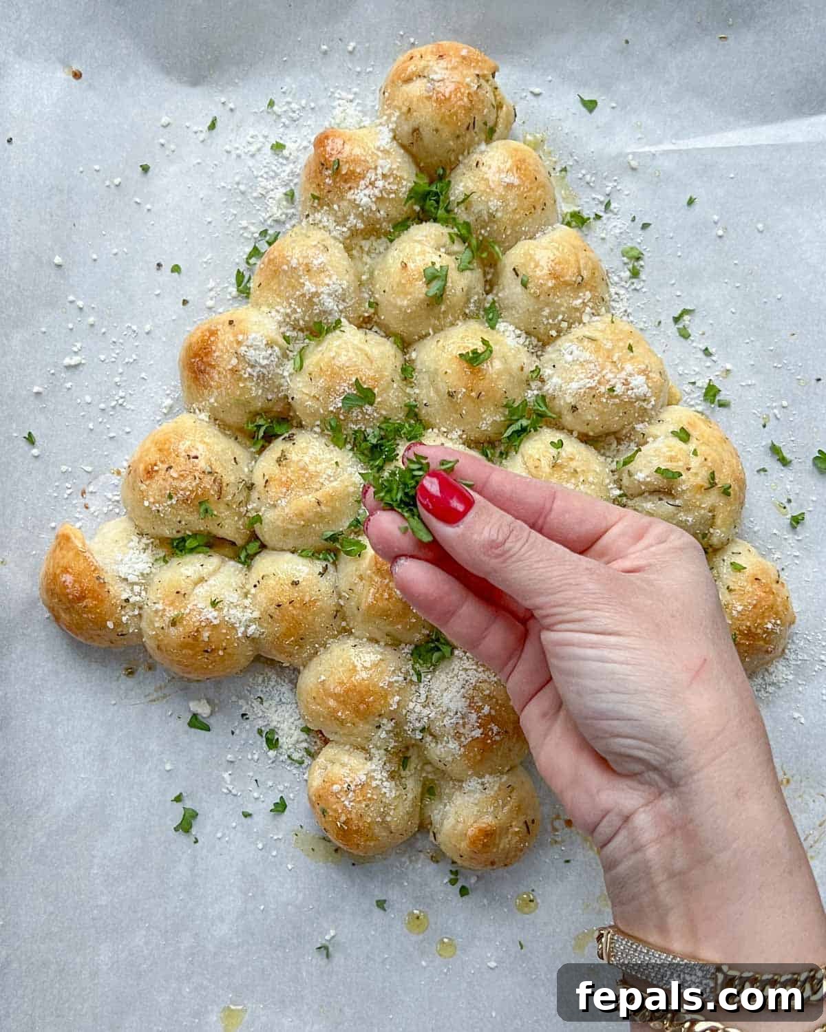 Fresh parsley and grated Parmesan cheese being sprinkled over the herb-brushed, baked Christmas tree pull-apart bread for garnish.