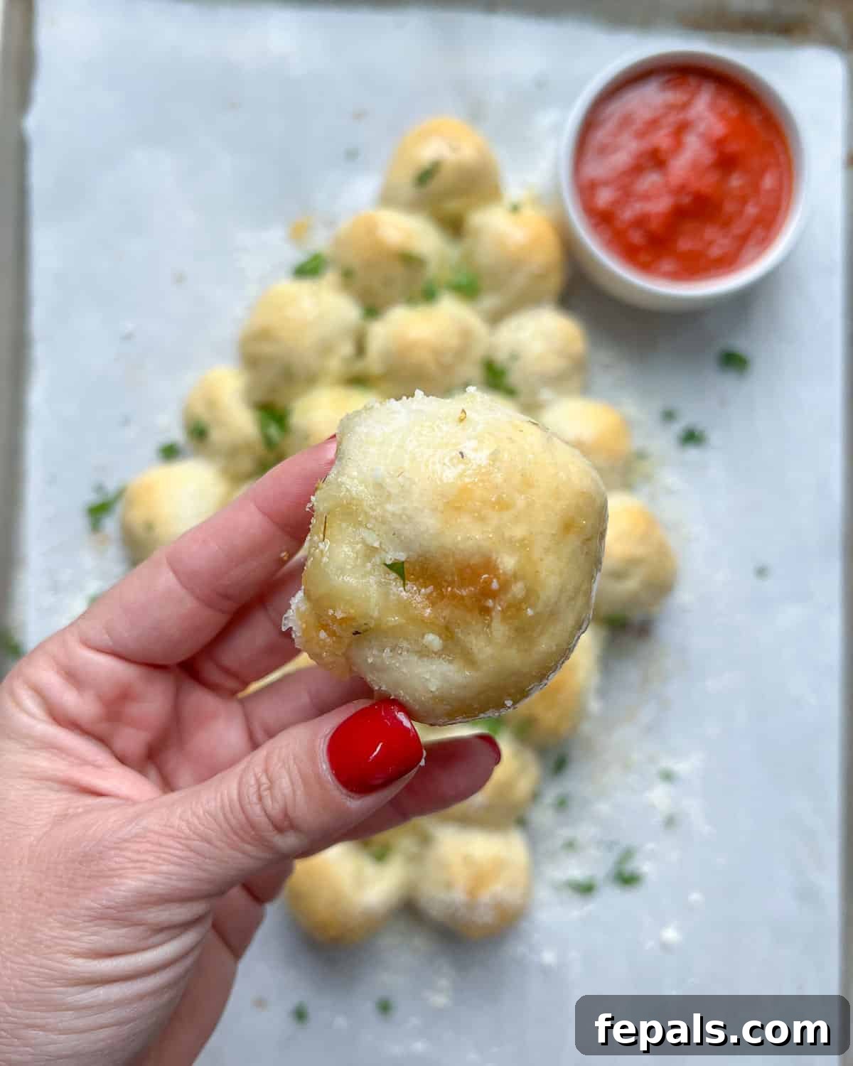 A hand gently holding a single, golden-brown pull-apart cheese ball, highlighting its soft texture and cheesy filling.