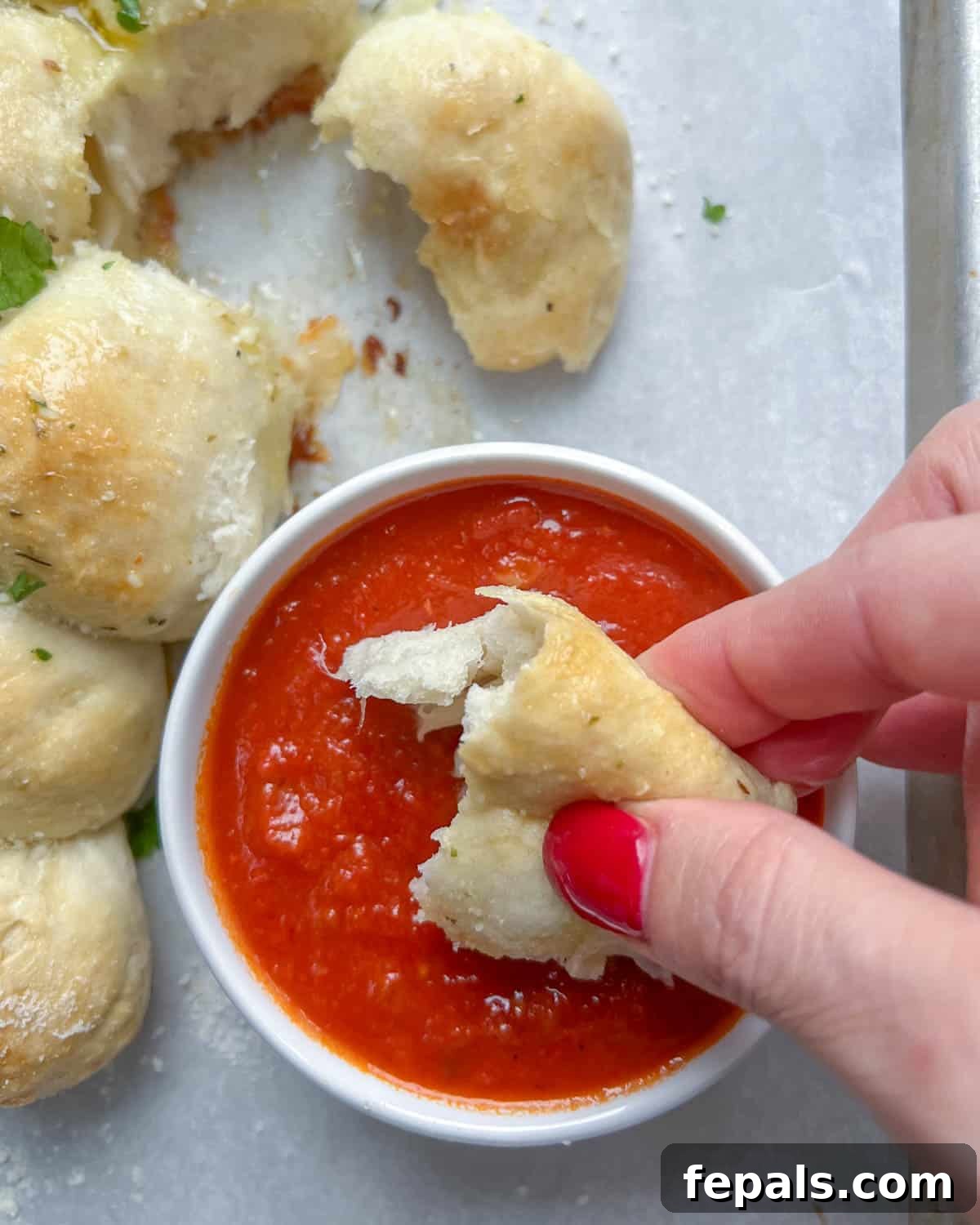 A golden, baked cheese pull-apart bread ball being dipped into a bowl of rich marinara sauce, perfect for sharing.