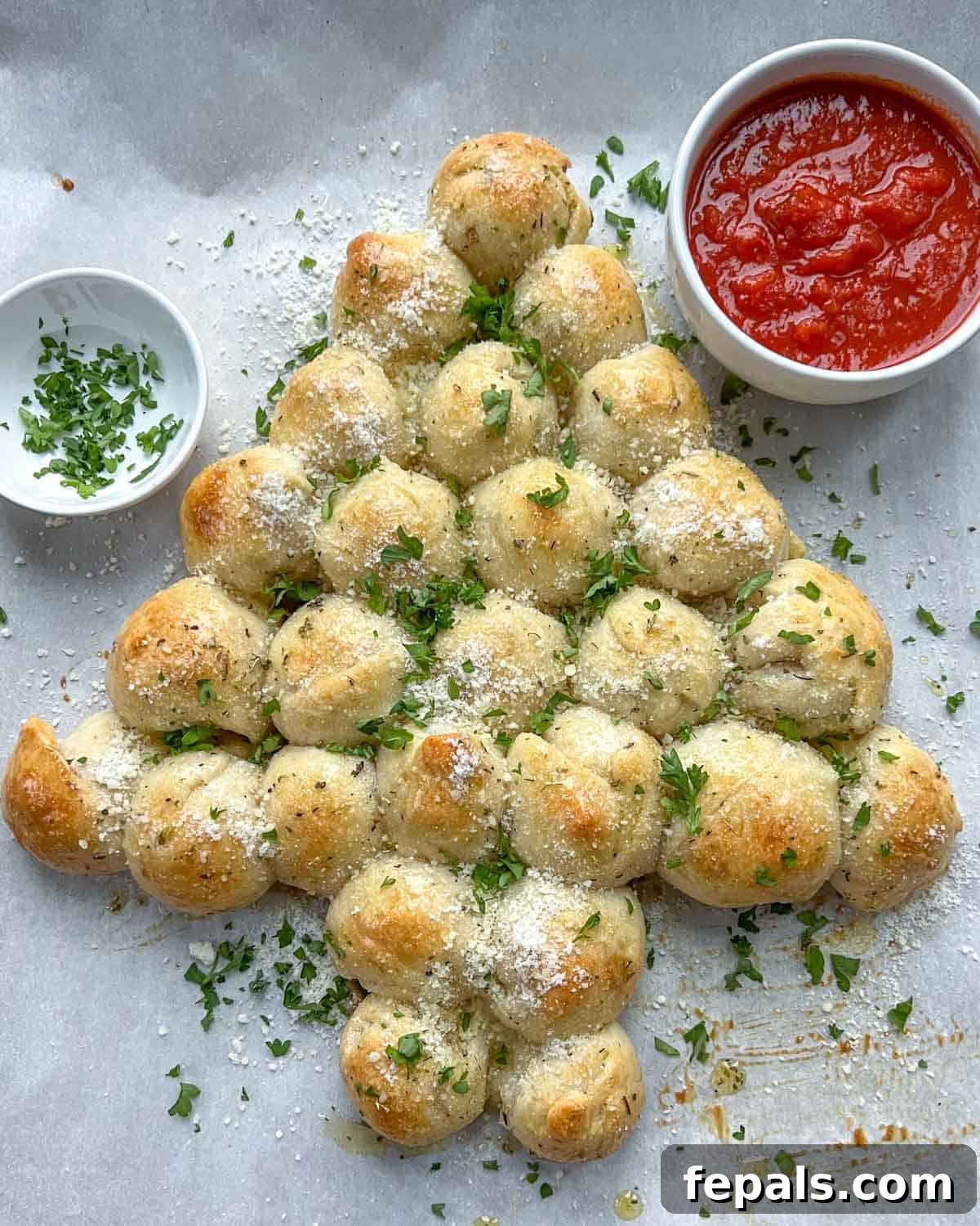 The fully baked and garnished Christmas tree pull-apart bread, presented on a sheet pan with a bowl of marinara sauce, ready to be enjoyed.