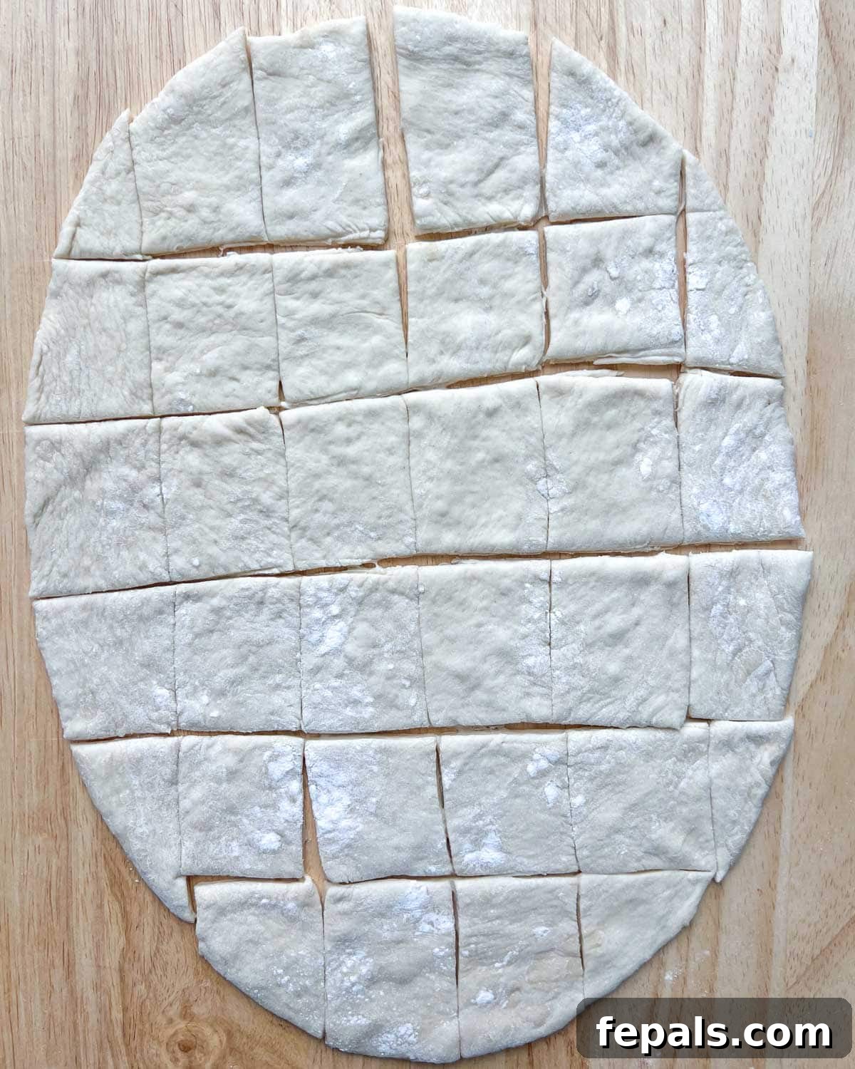 Pizza dough neatly cut into small, even square sections, prepared for stuffing with cheese.