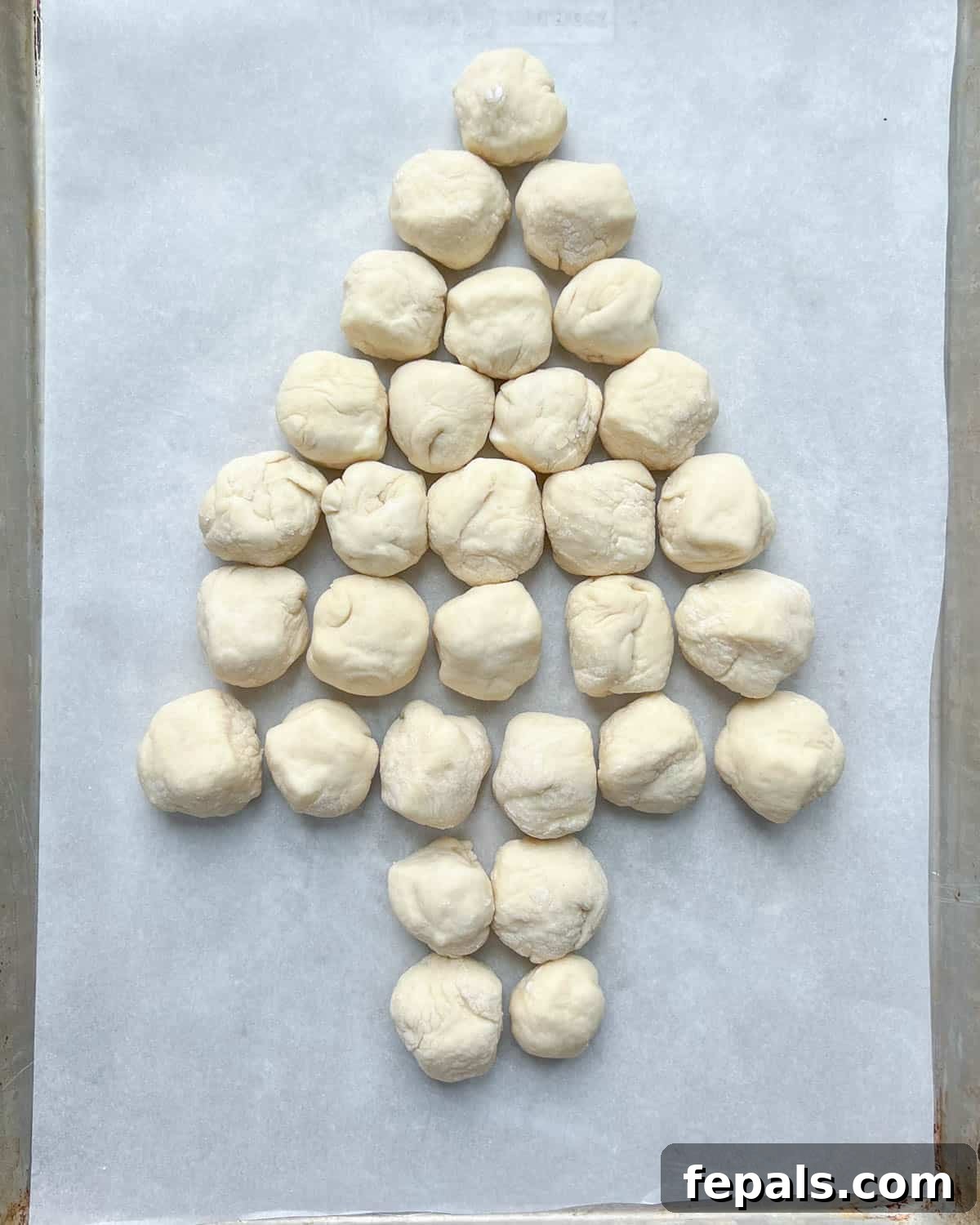 Cheese-stuffed dough balls arranged on a parchment-lined baking sheet in the distinctive shape of a Christmas tree, ready for the oven.