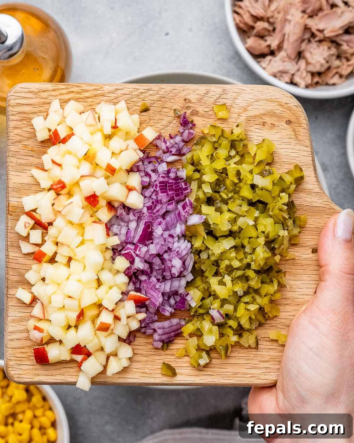 The McConaughey Tuna Salad That Broke the Internet 5 Cutting board featuring neatly chopped fresh apple, crisp red onion, tangy dill pickles, and crushed crispy jalapeño chips, prepared for the salad.