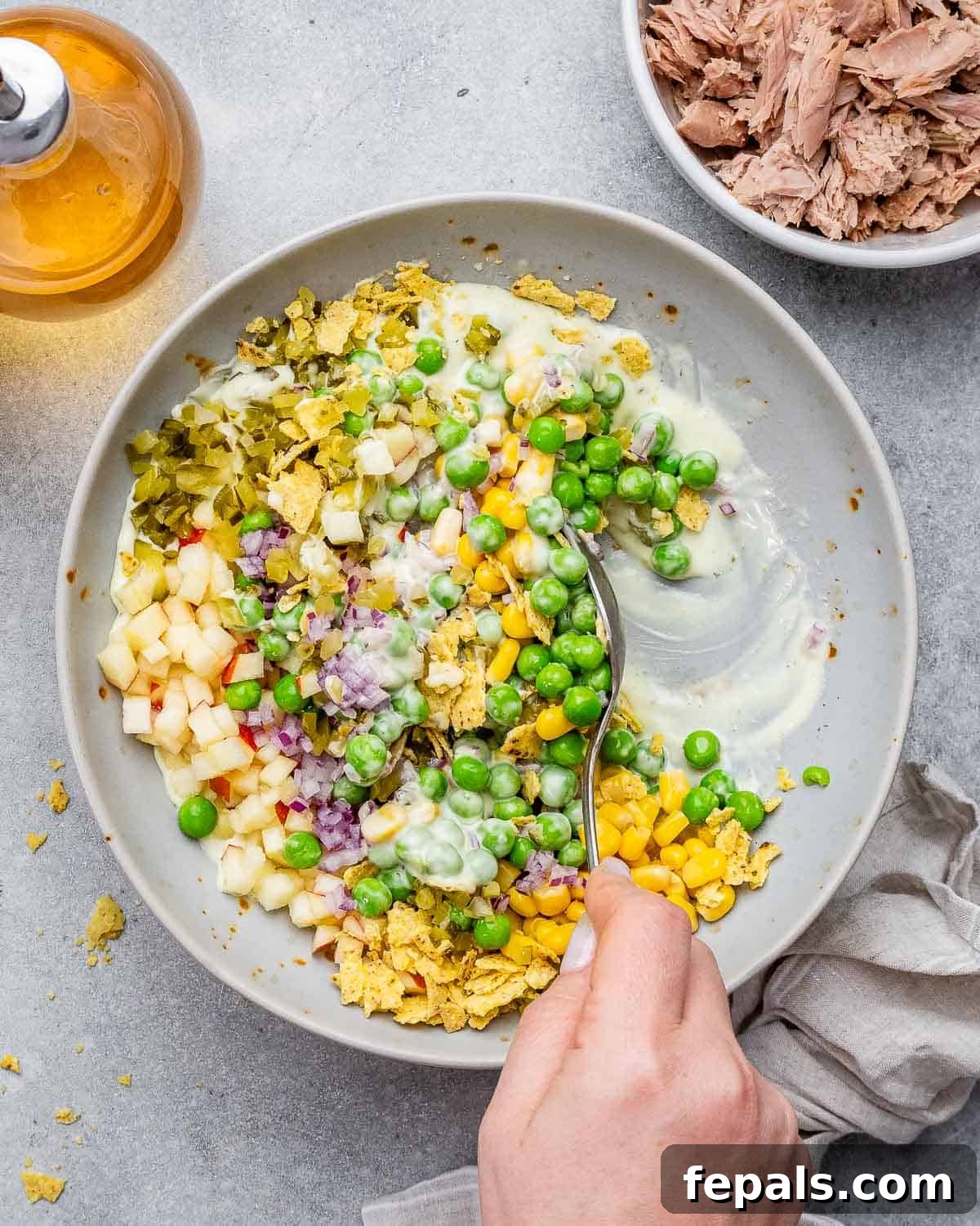 The McConaughey Tuna Salad That Broke the Internet 7 A spoon actively mixing all the vibrant ingredients into the creamy dressing within a large bowl, ensuring everything is thoroughly coated.