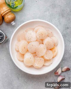 Fresh raw scallops in a white bowl, seasoned with salt and pepper, ready to be cooked.