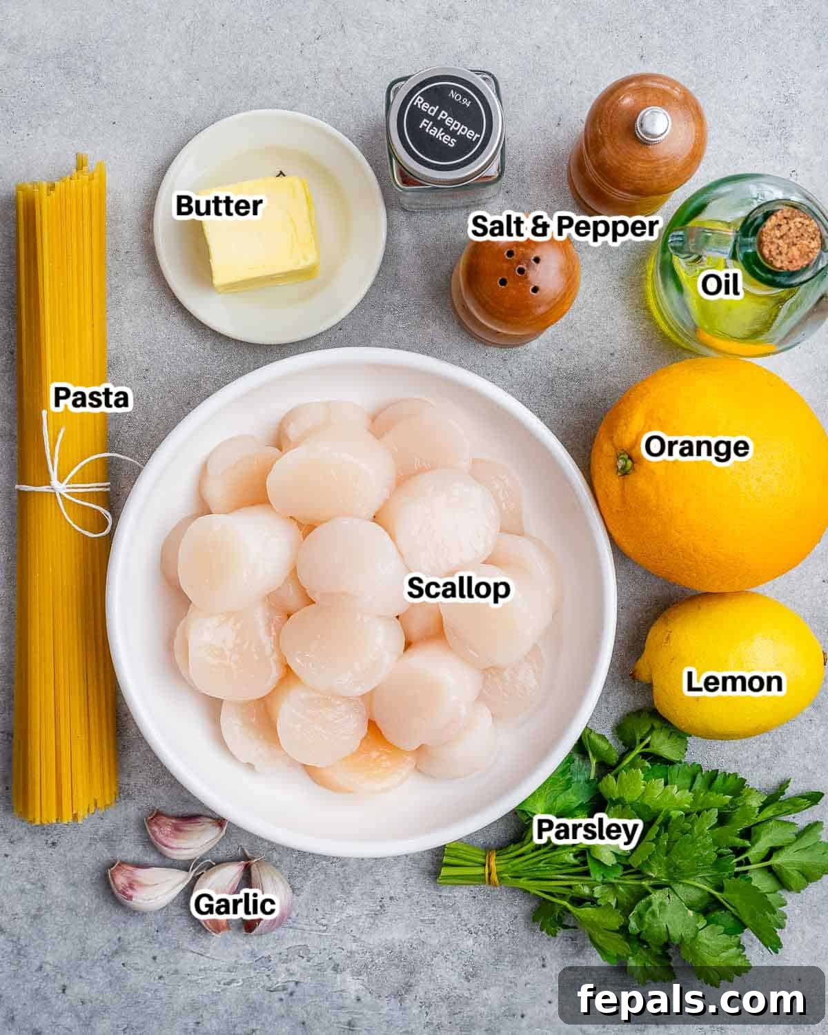A vibrant display of fresh ingredients for scallop pasta including scallops, lemons, oranges, garlic, butter, and herbs.