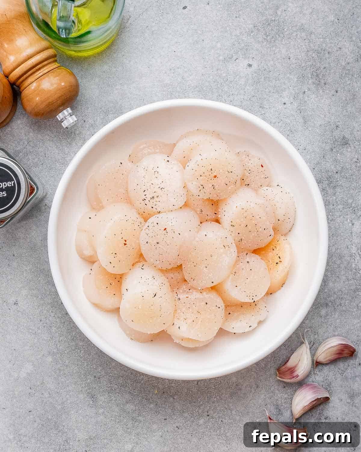 Fresh raw scallops in a white bowl, seasoned with salt and pepper, ready to be cooked for scallop pasta.