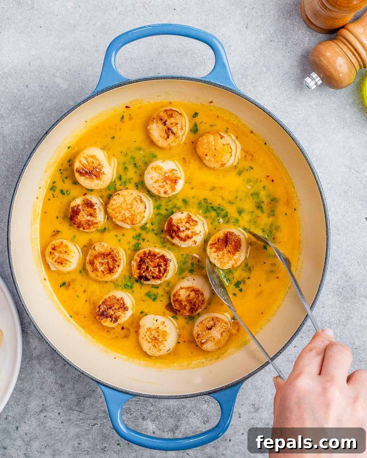 Tongs gently placing perfectly seared scallops back into the pan with the bubbling citrus garlic sauce, infusing flavors.