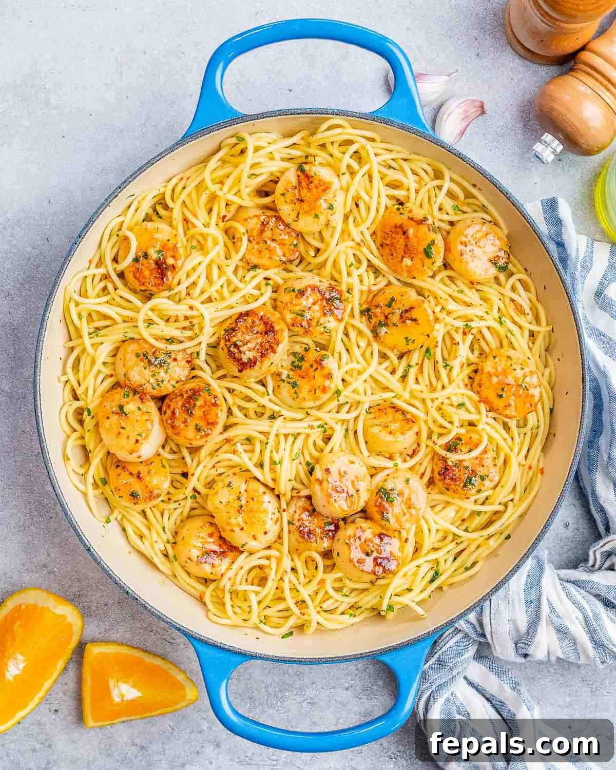 Cooked pasta and golden-seared scallops tossed together in a large skillet, fully coated in the bright citrusy sauce, ready to be served.