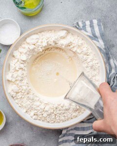 Perfect Italian Focaccia At Home 14 Pouring activated yeast, sugar, salt, and water over a bowl of flour.