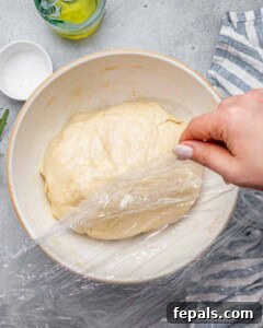 Perfect Italian Focaccia At Home 15 Top view of focaccia dough ball in bowl with plastic wrap.