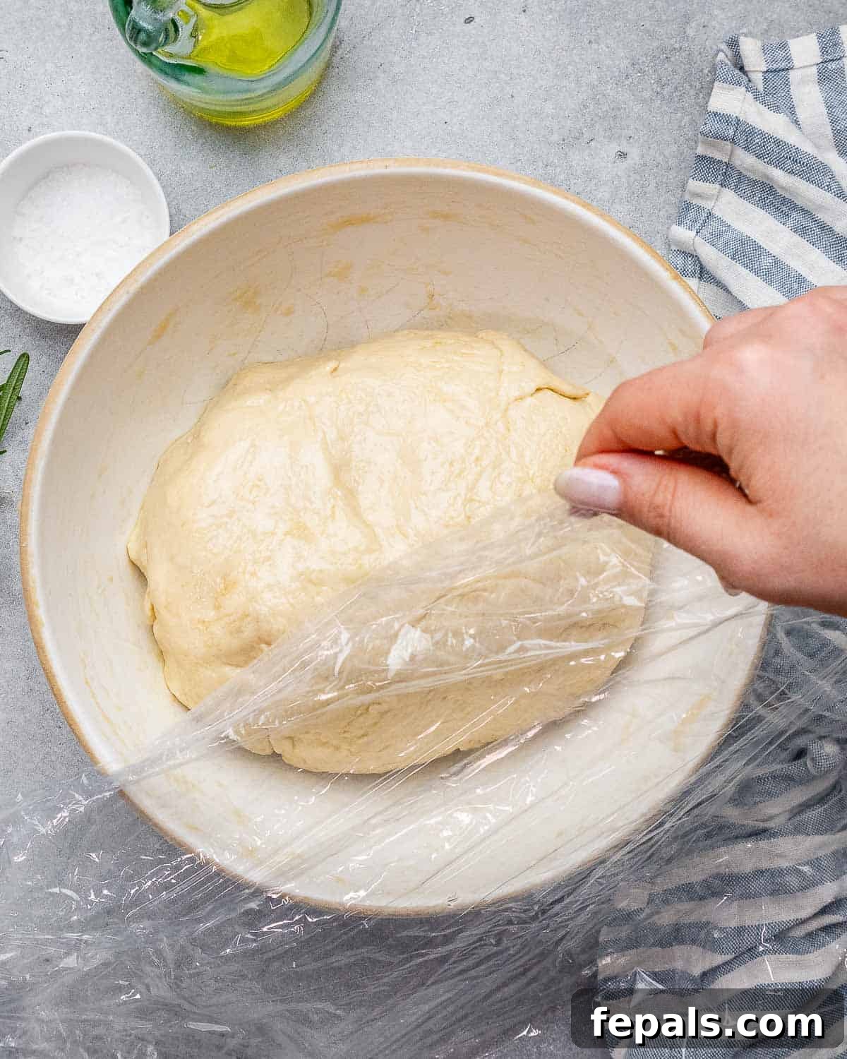 Perfect Italian Focaccia At Home 6 Focaccia dough rising in a bowl under plastic wrap.