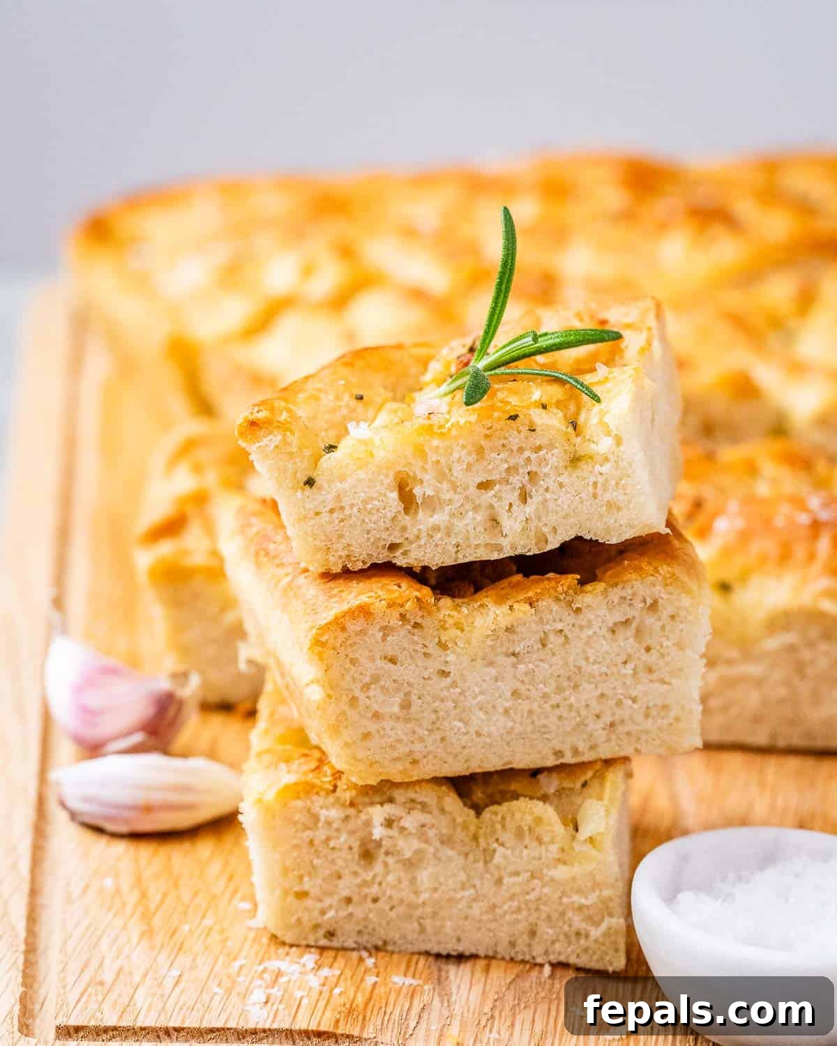 Perfect Italian Focaccia At Home 9 Three slices of focaccia bread with rosemary and garlic on a wooden cutting board.