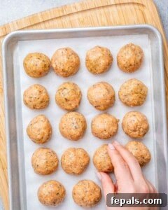 Rolled chicken meatballs on a large baking sheet.