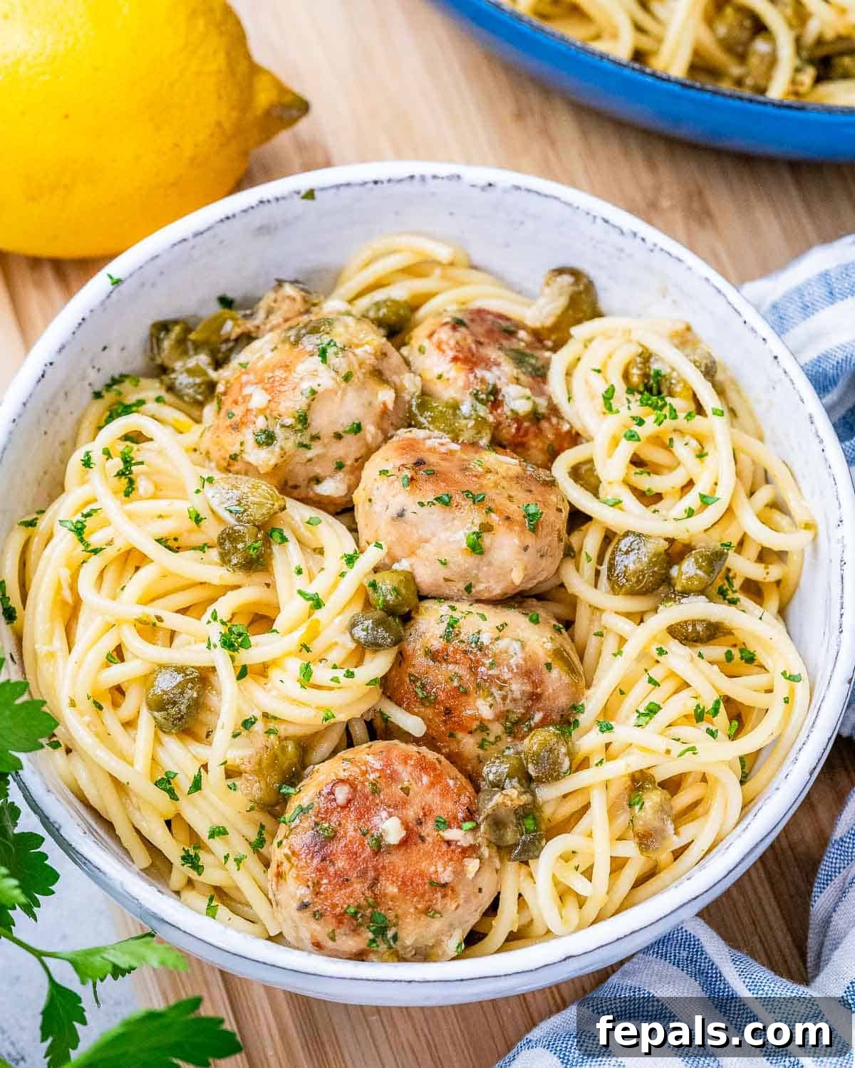 A white bowl filled with spaghetti pasta and topped with golden-brown chicken piccata meatballs and parsley.