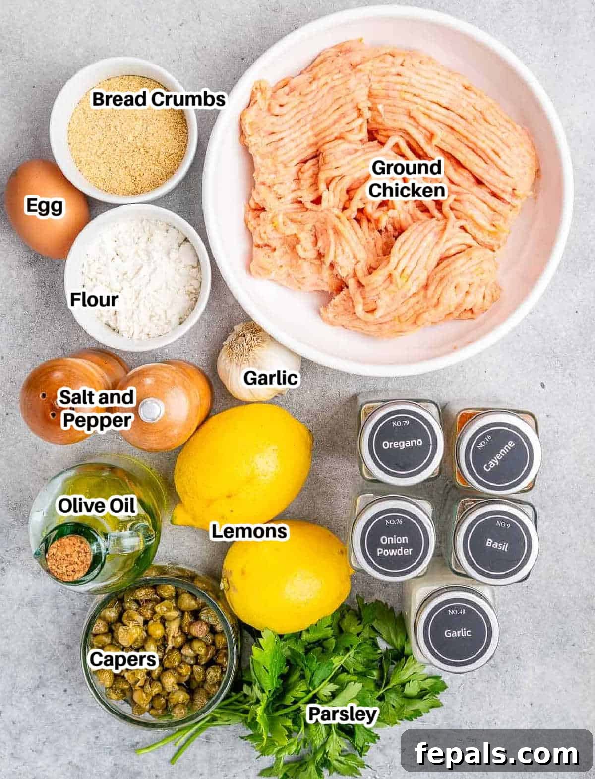 A flat lay of fresh ingredients to make chicken piccata meatballs, including ground chicken, lemons, capers, and herbs.