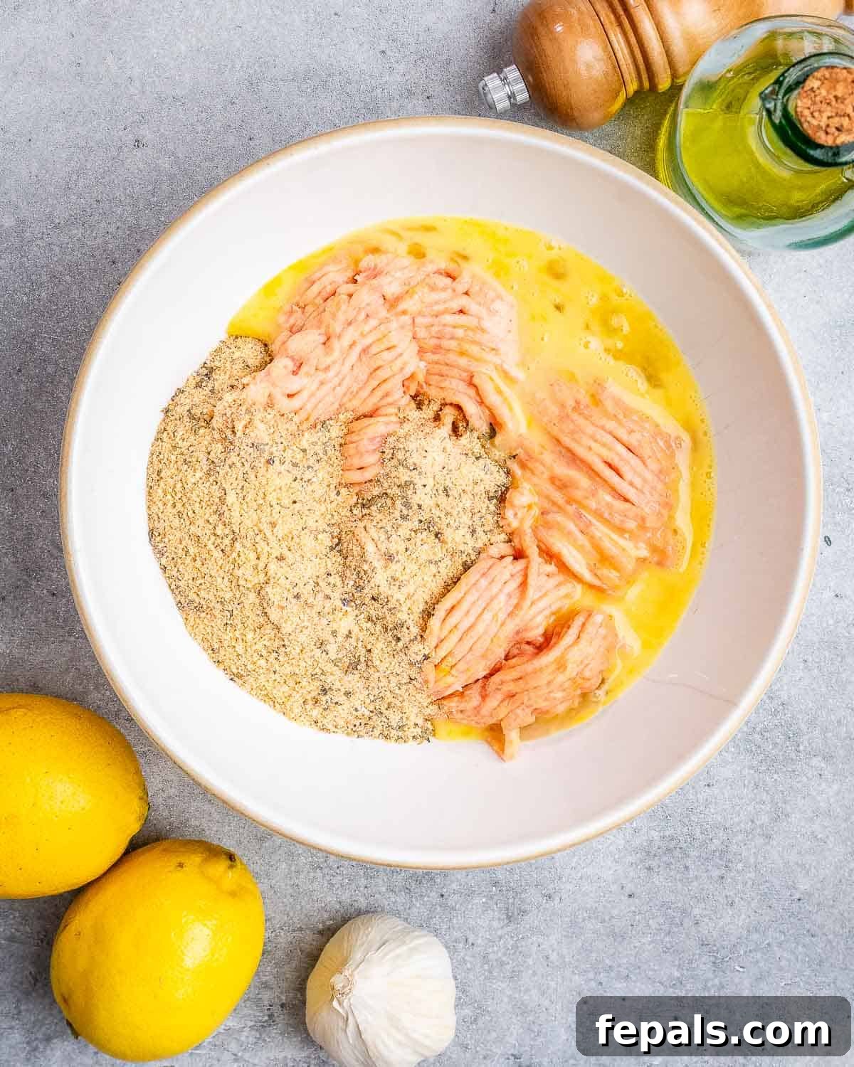 A bowl filled with ground chicken and other ingredients being mixed to form meatballs.