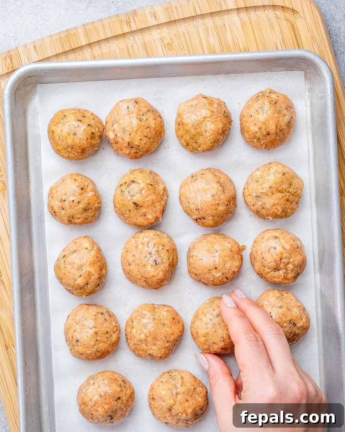 Rolled chicken meatballs, lightly dredged in flour, arranged on a large baking sheet, ready for searing.