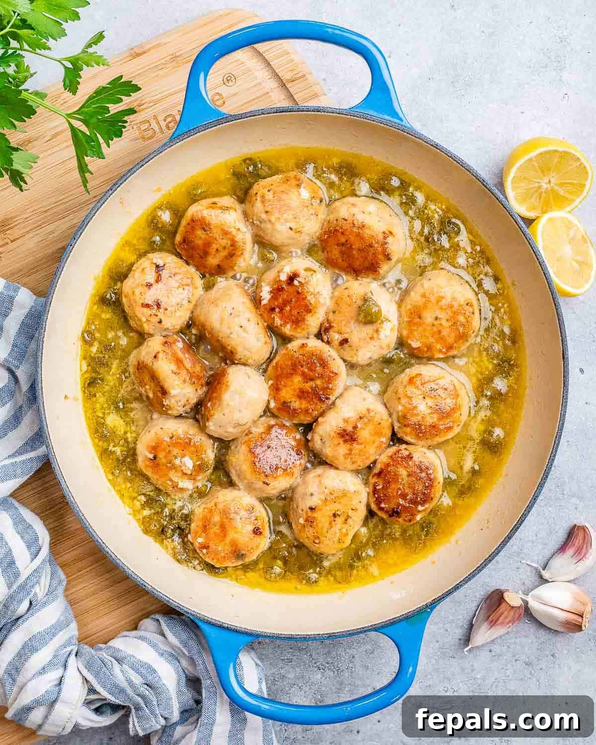Golden-brown chicken meatballs simmering in a vibrant lemon-caper piccata sauce in a pot on the stove.