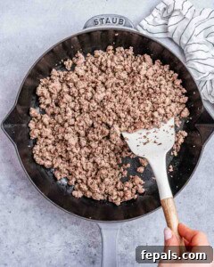 Ground sausage in a cast iron skillet stirred by a spatula.