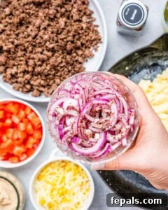 A hand holding a bowl of sliced onions over the ingredients to make burritos.